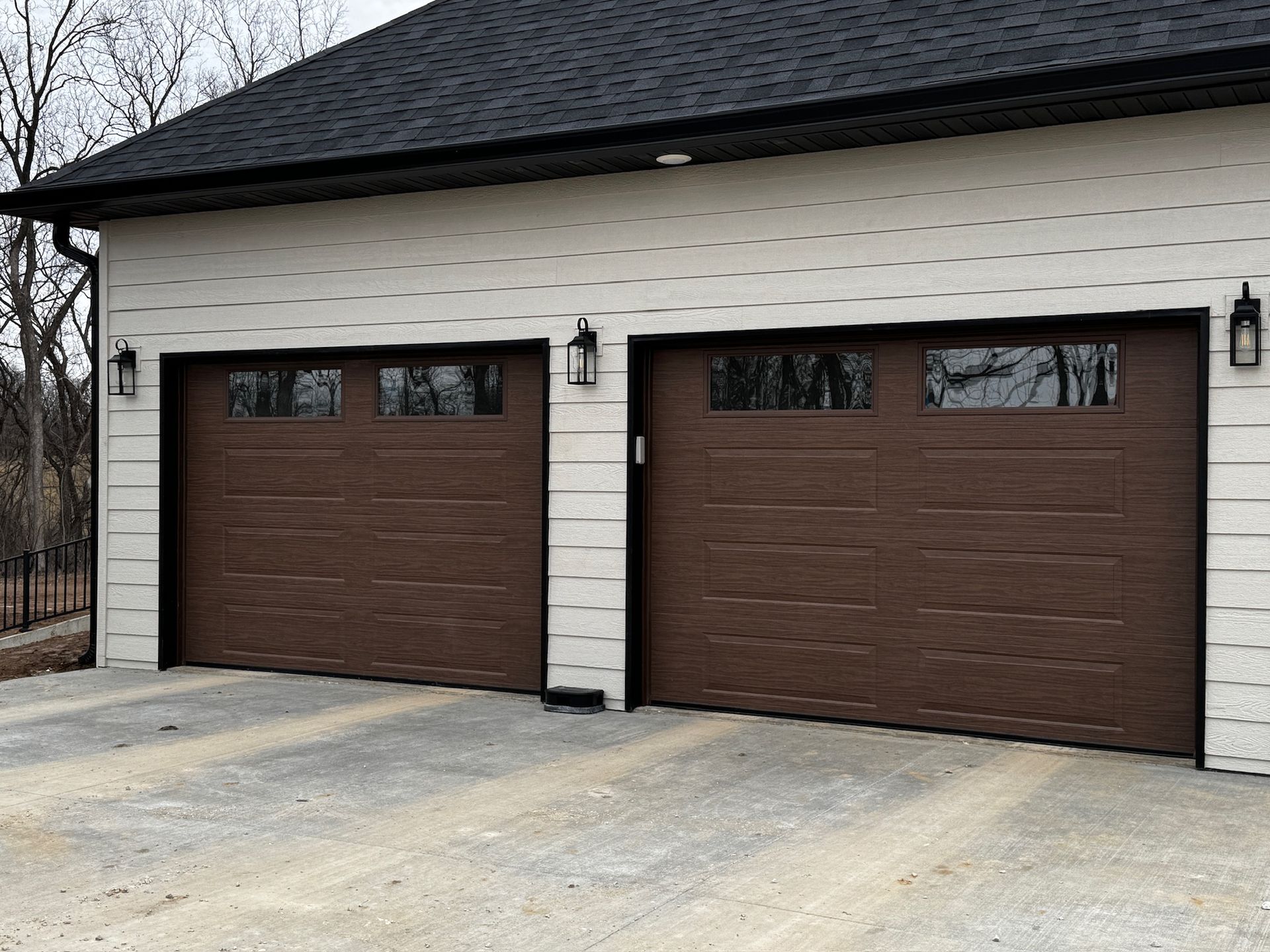 Two brown garage doors on a beige house with a concrete driveway