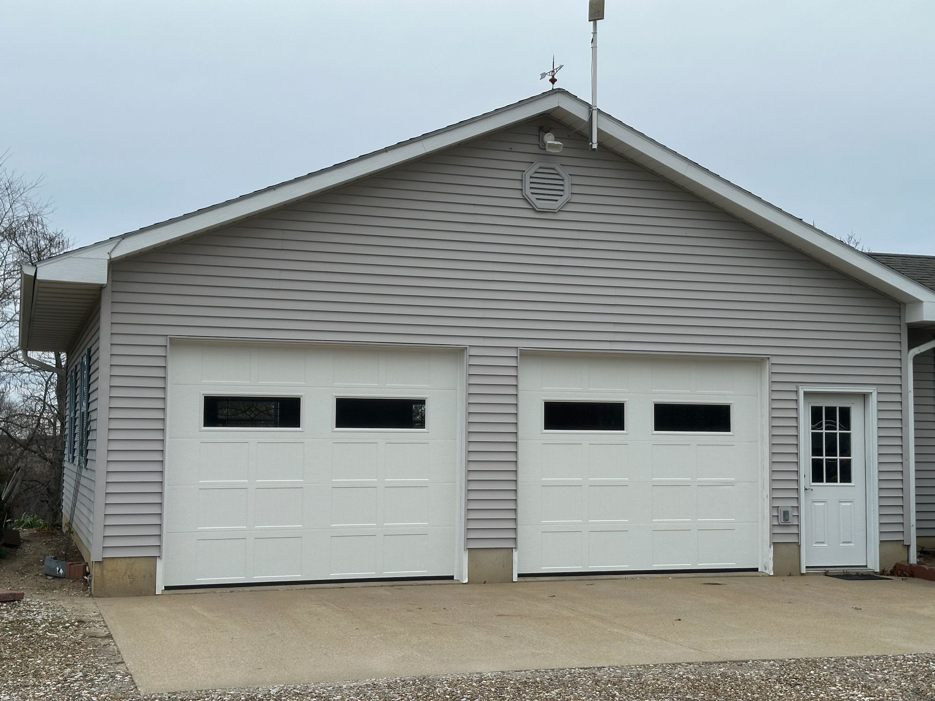 Two-car garage with white doors and siding, a side door, and a light-colored driveway under an overcast sky.