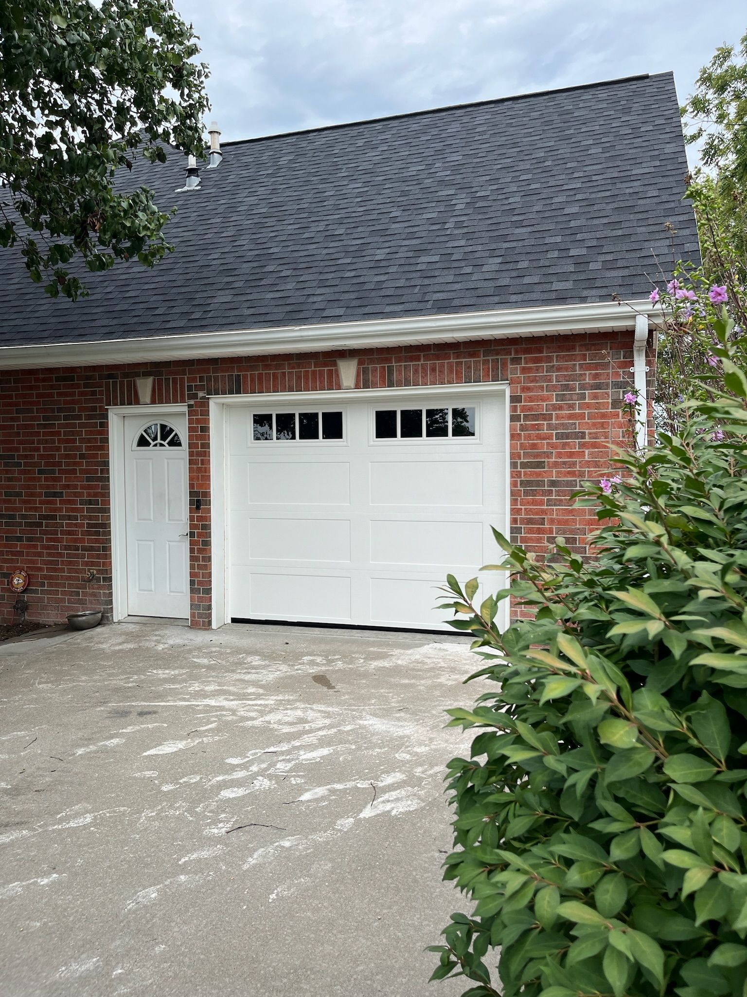 White garage door and side door in a brick building with a dark roof and concrete driveway.