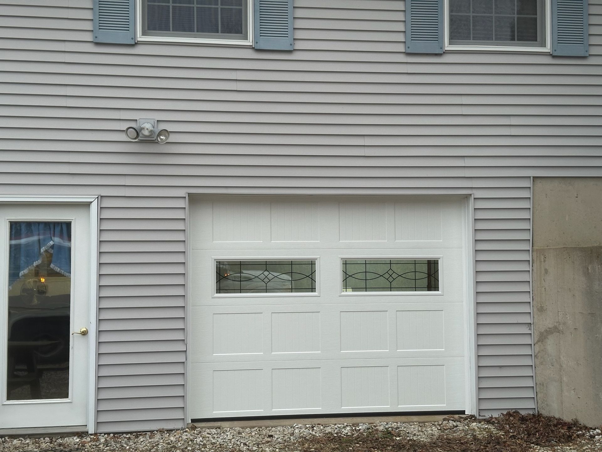 White garage door with window panels and a side door on a gray house.