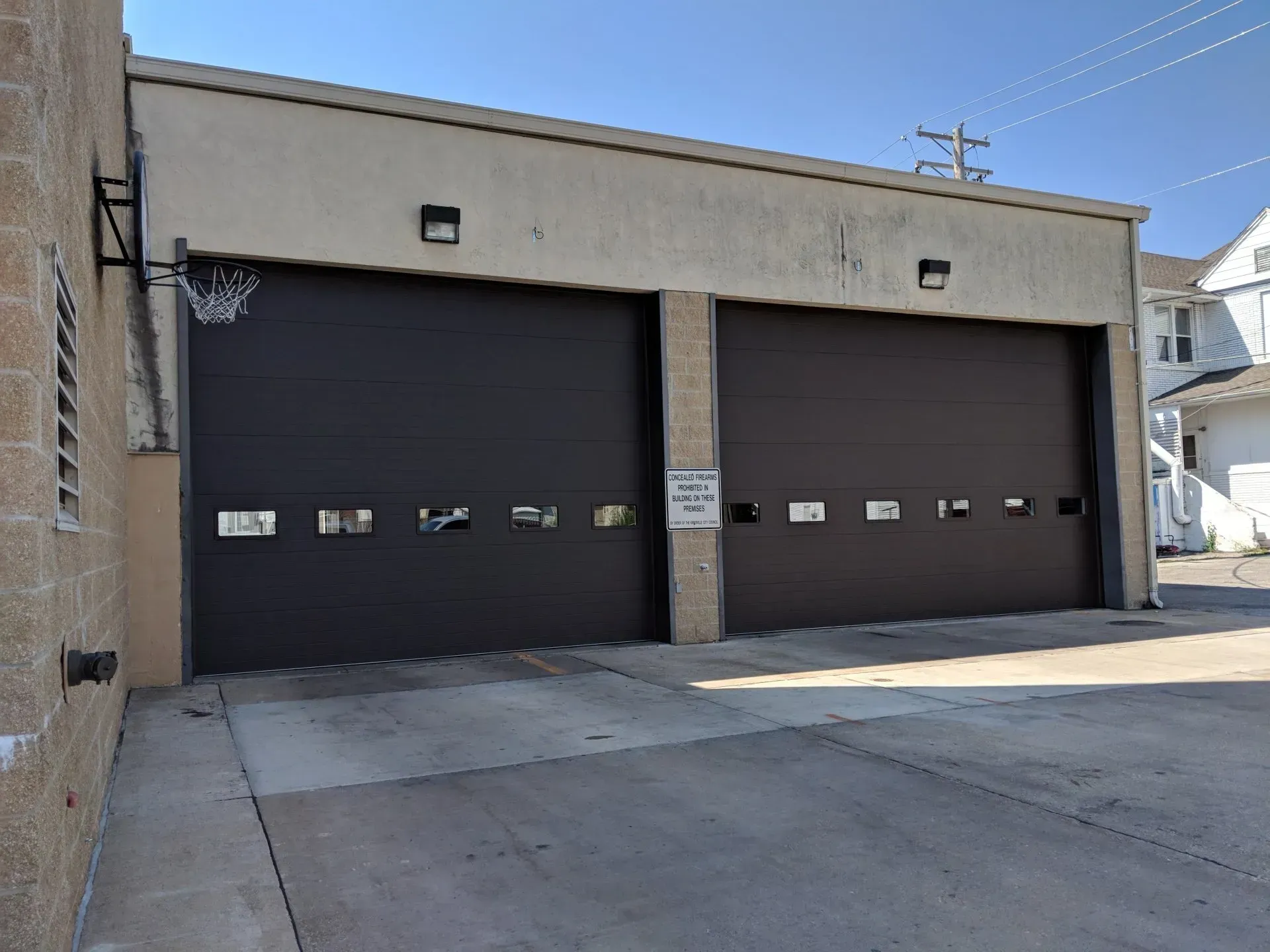 Two brown garage doors on a light beige building with a basketball hoop.