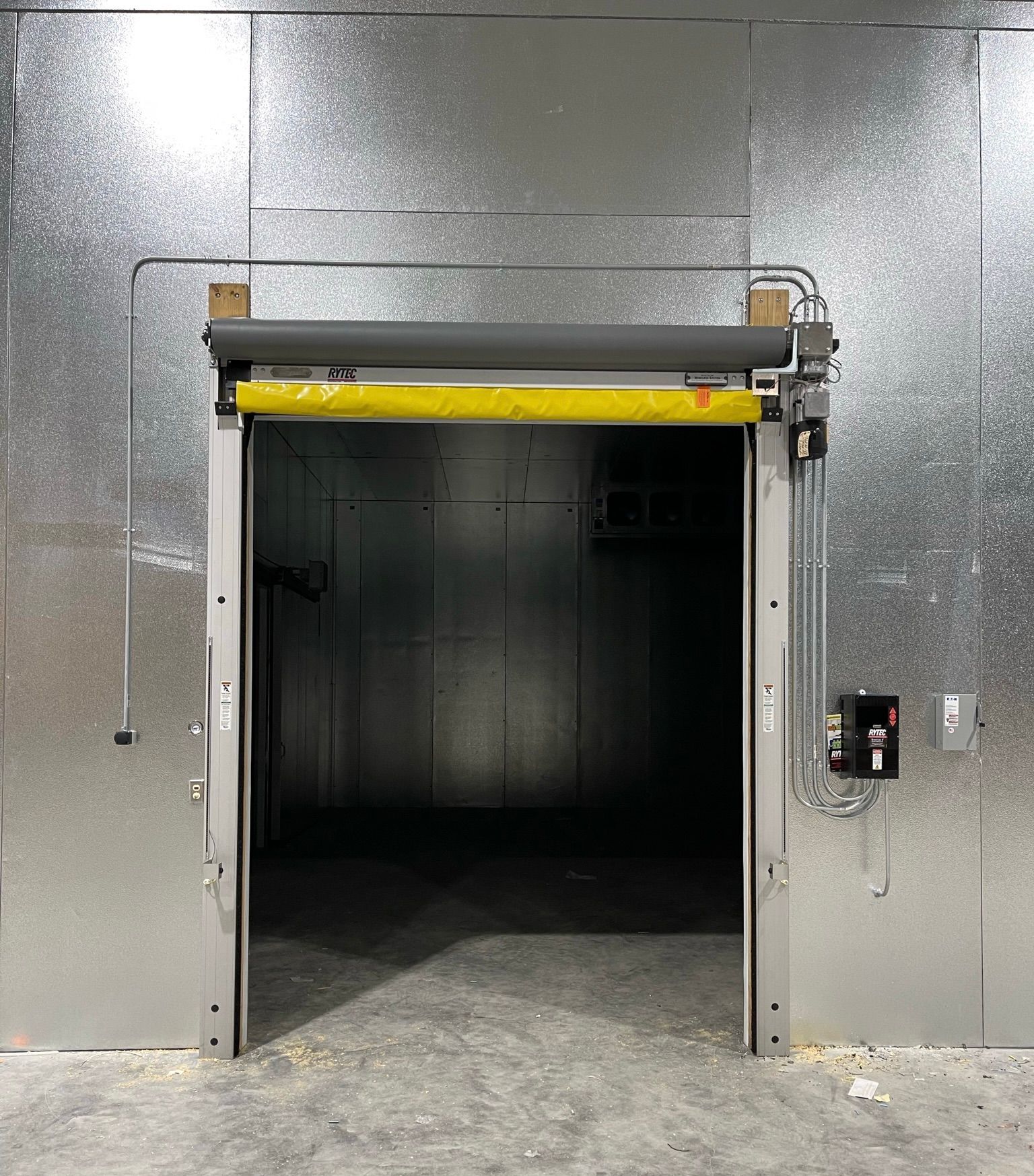 Industrial loading dock doorway with a yellow roll-up door and control panel on a gray wall