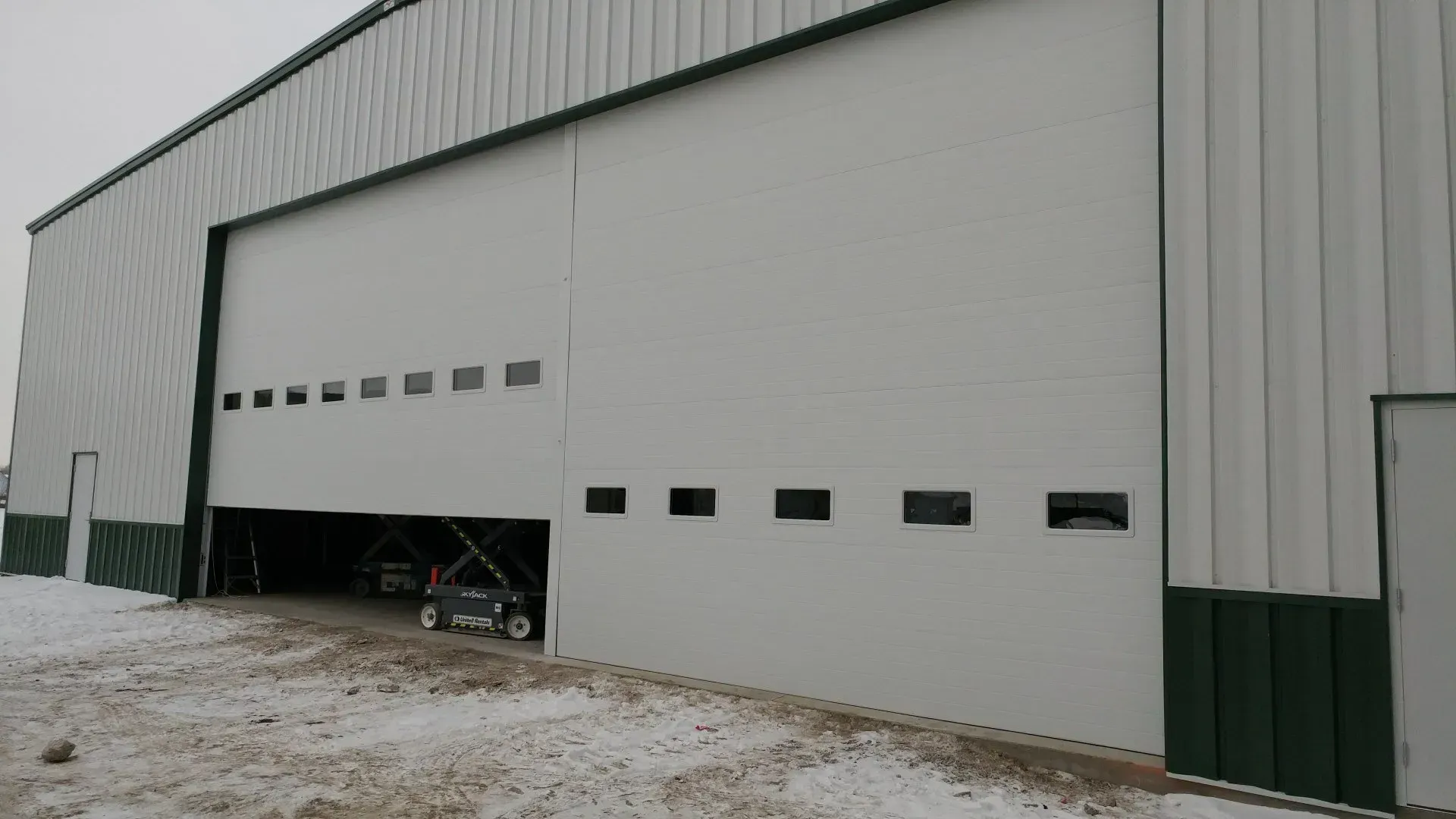 White industrial sliding door partially open on a building, a vehicle is visible inside the building.