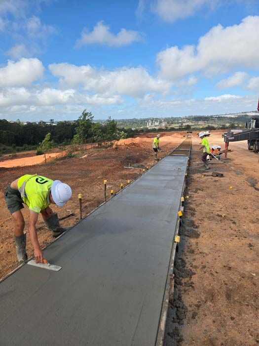 Workers pouring concrete for a long sidewalk on a construction site under a blue sky
