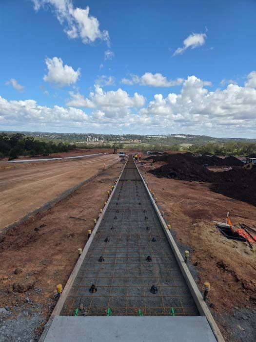 Long concrete road under construction through a barren landscape, with blue sky and clouds above