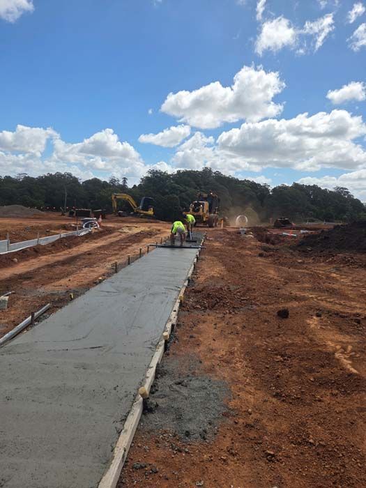 Construction workers paving a new concrete road under a cloudy sky