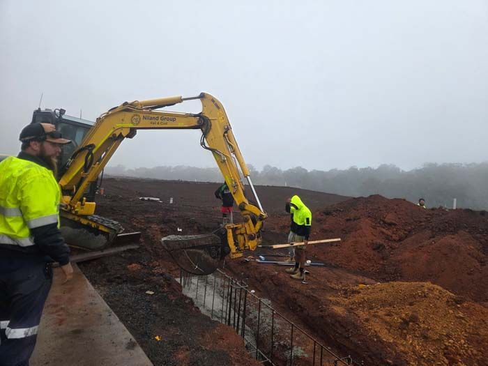 Construction workers and excavator digging a trench on a muddy site in overcast weather