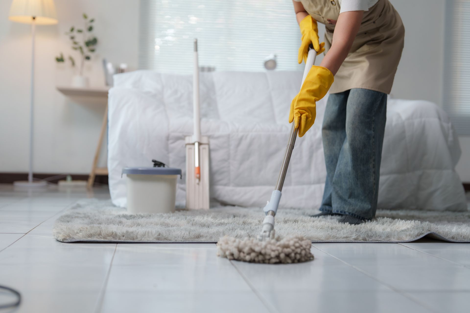 Person mopping a white rug in a bright living room, wearing yellow gloves.