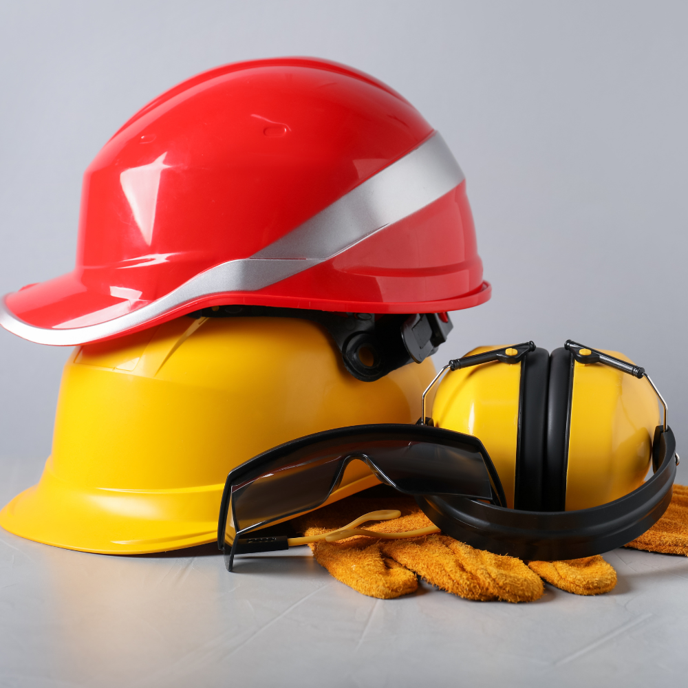 Red and yellow hard hats beside black safety glasses and work gloves on a gray surface