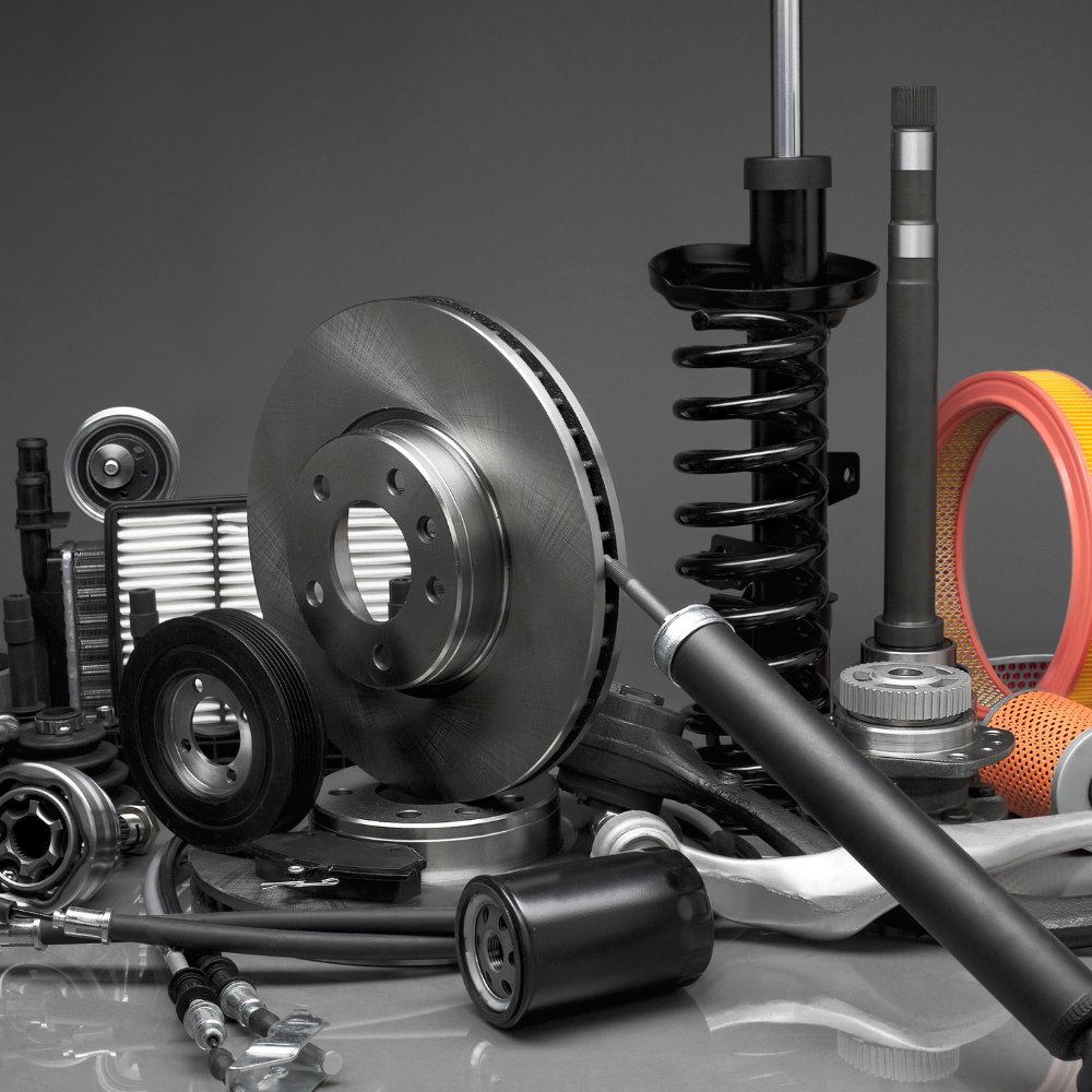 Assorted car parts and tools, including a brake disc, shock absorber, belts, and a tire, on a gray background