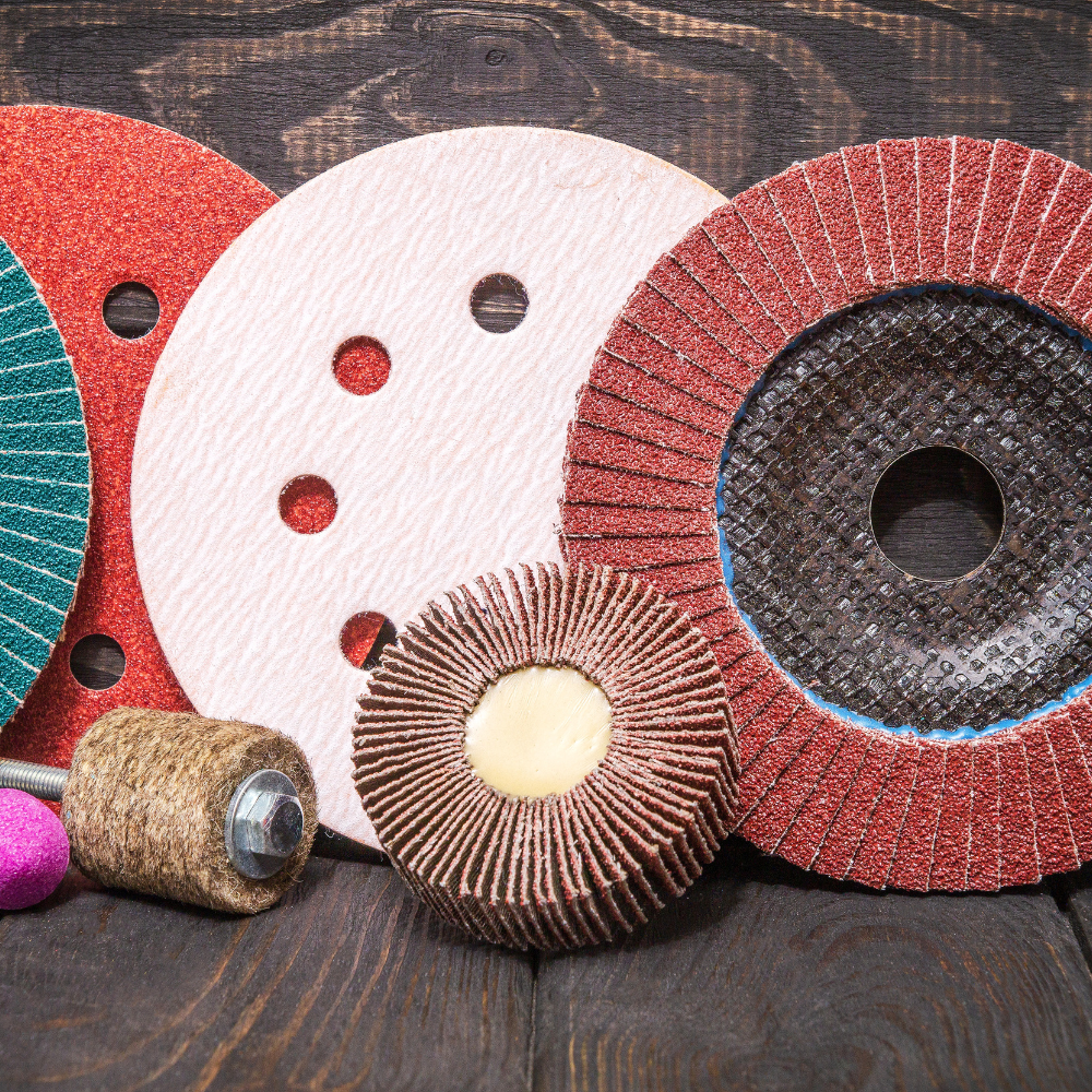 Assorted abrasive sanding discs and drum sleeves in red, white, and brown on a dark wood surface