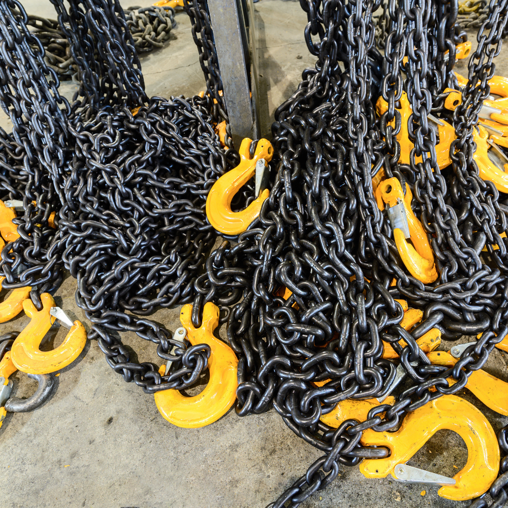 Black chains with bright yellow hooks piled on a concrete floor.