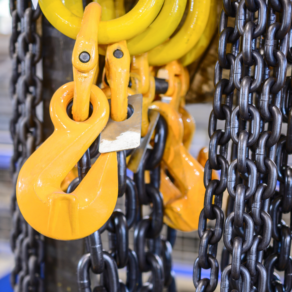 Yellow and black industrial chain hooks hanging against a background of heavy chains