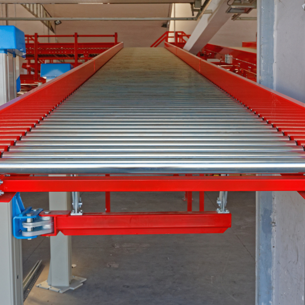 Red roller conveyor system in an industrial warehouse, viewed from the end of the line.