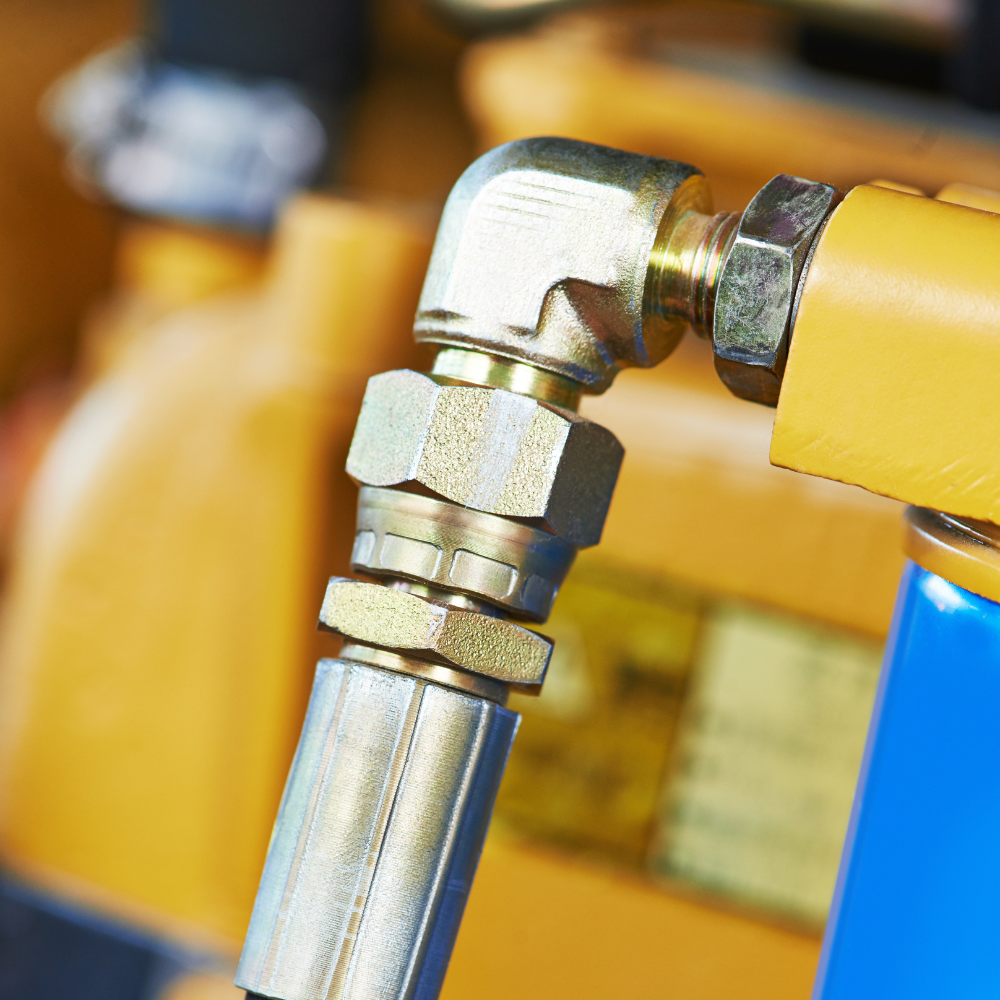 Yellow industrial hose connected to a metal elbow fitting and valve assembly