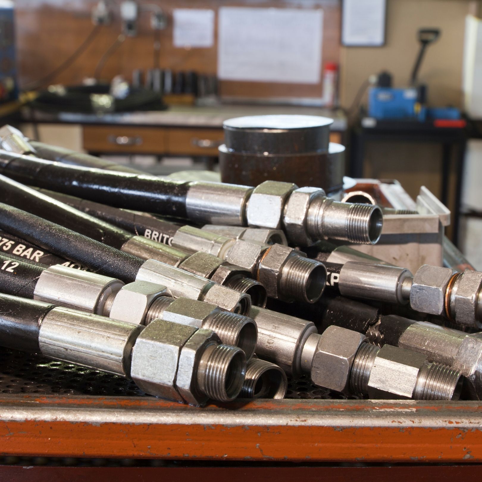 Pile of black hydraulic hoses with metal fittings on a workbench in a workshop