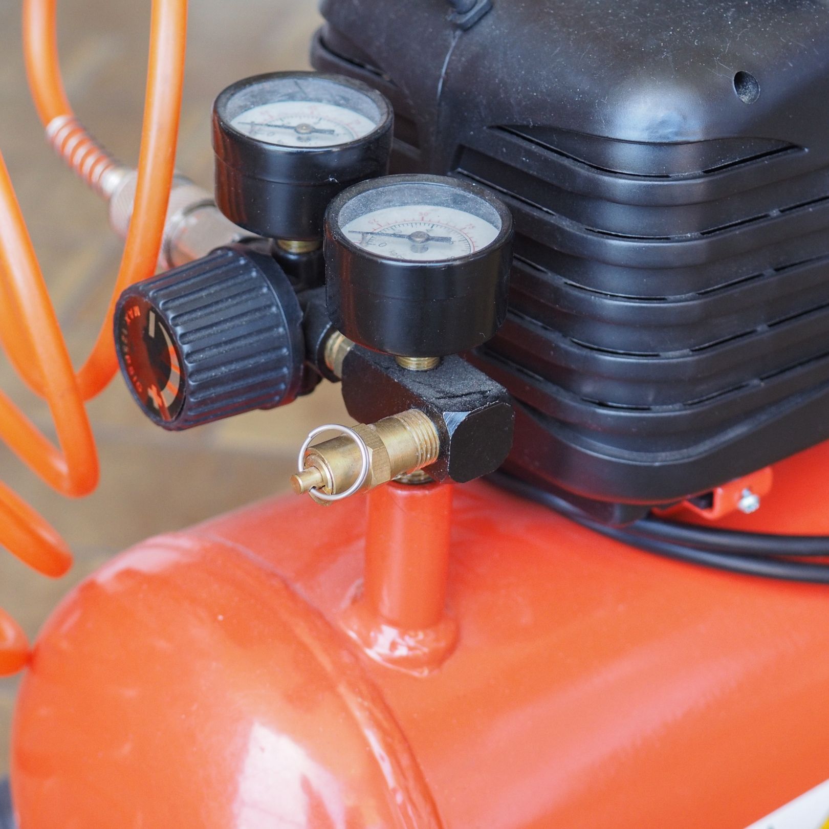 Close-up of an orange air compressor gauge and pressure controls with black knobs and hose fittings