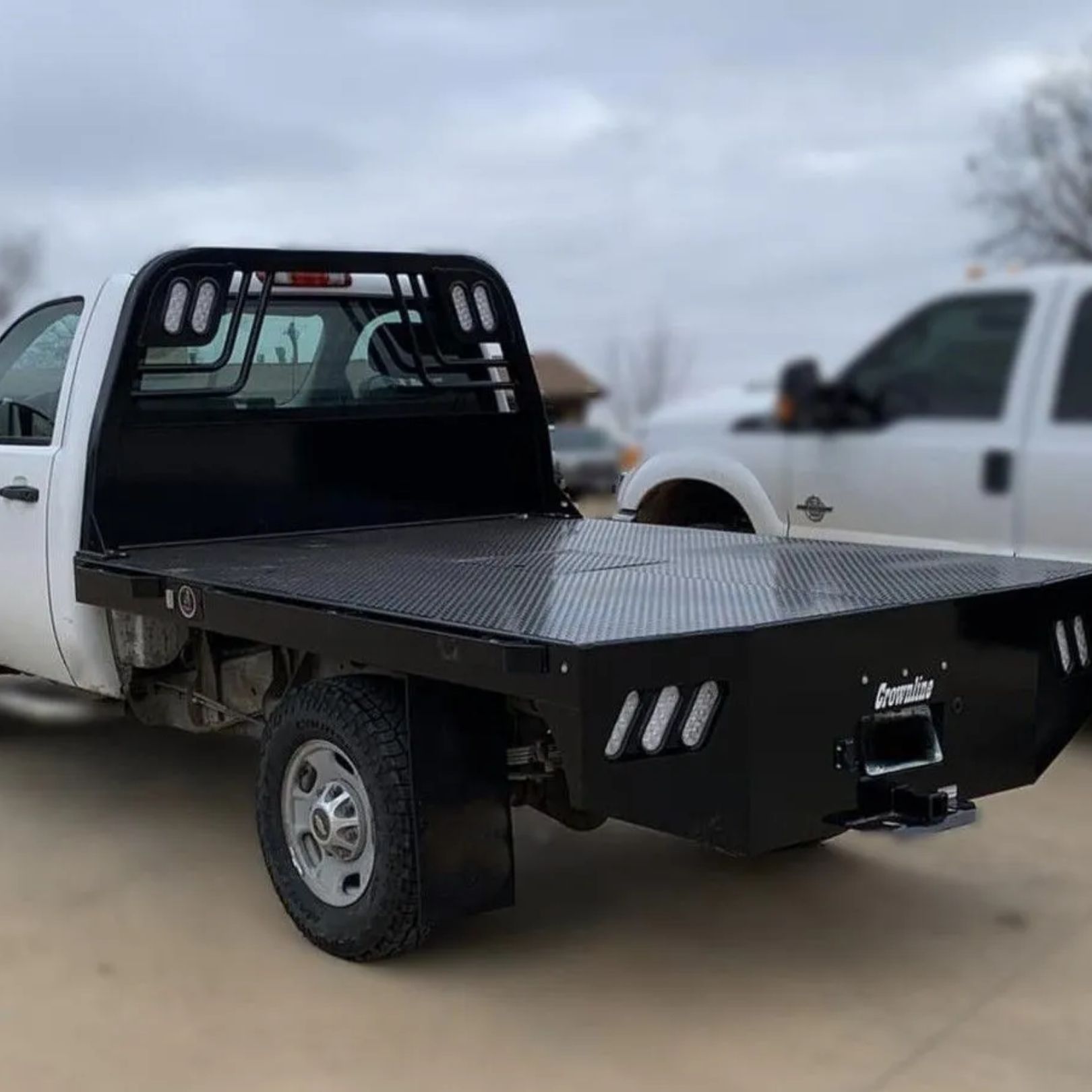 White flatbed pickup truck with black steel bed parked outdoors on a cloudy day