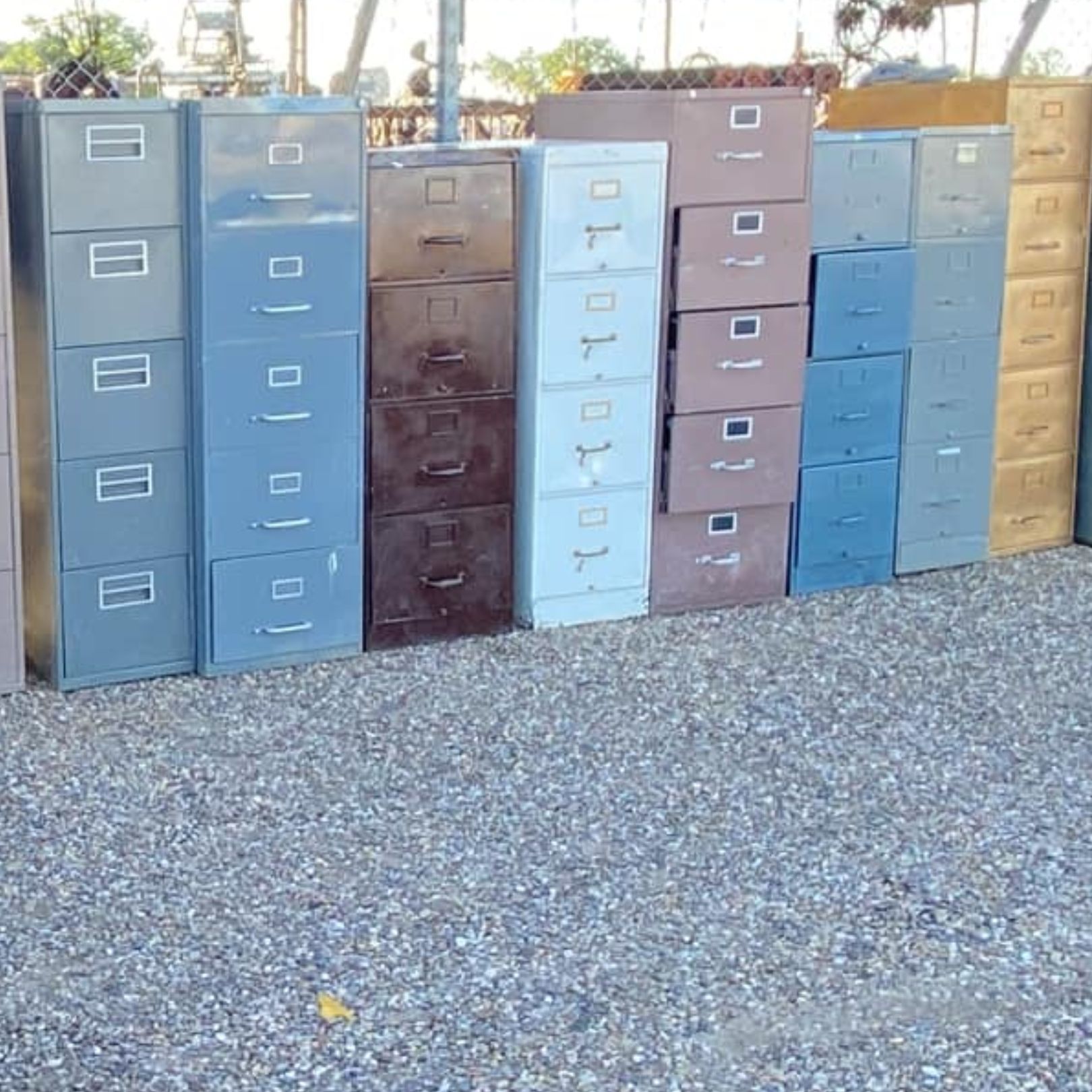 Row of colorful metal filing cabinets standing outdoors on gravel.