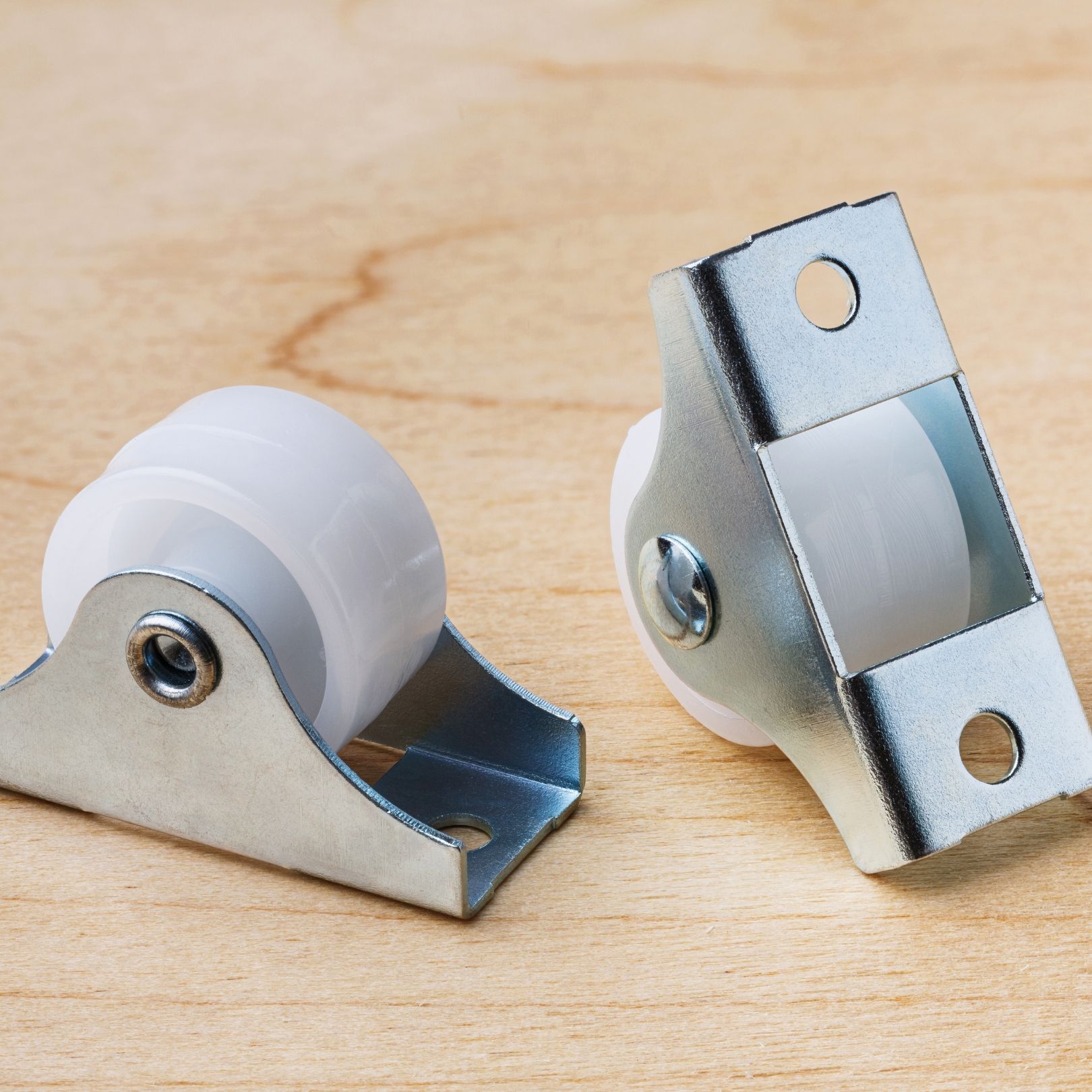Two small white roller wheel brackets on a wooden surface