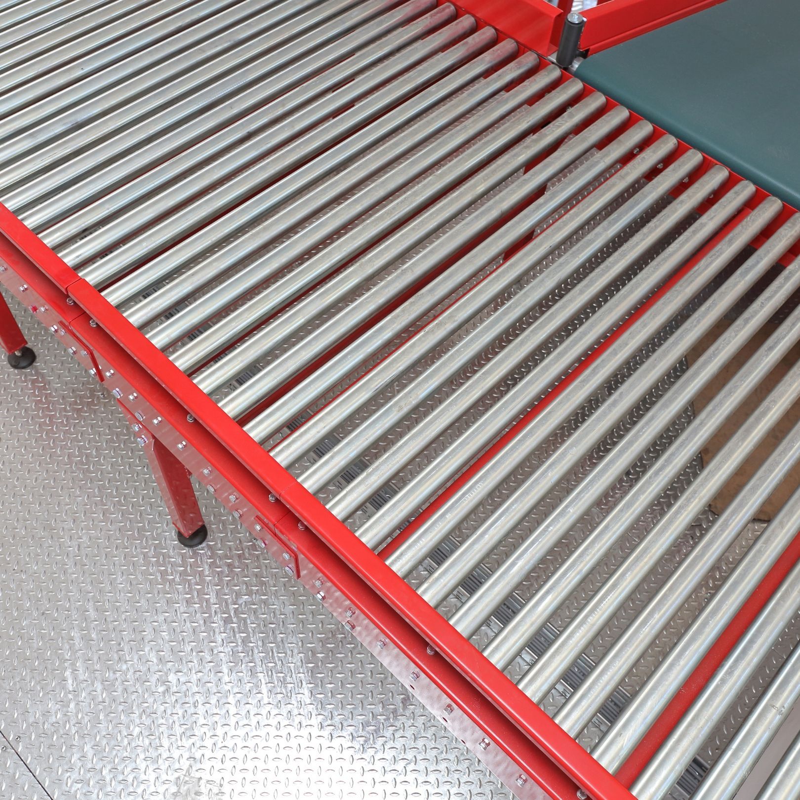 Red metal roller conveyor with silver rollers on a speckled gray floor