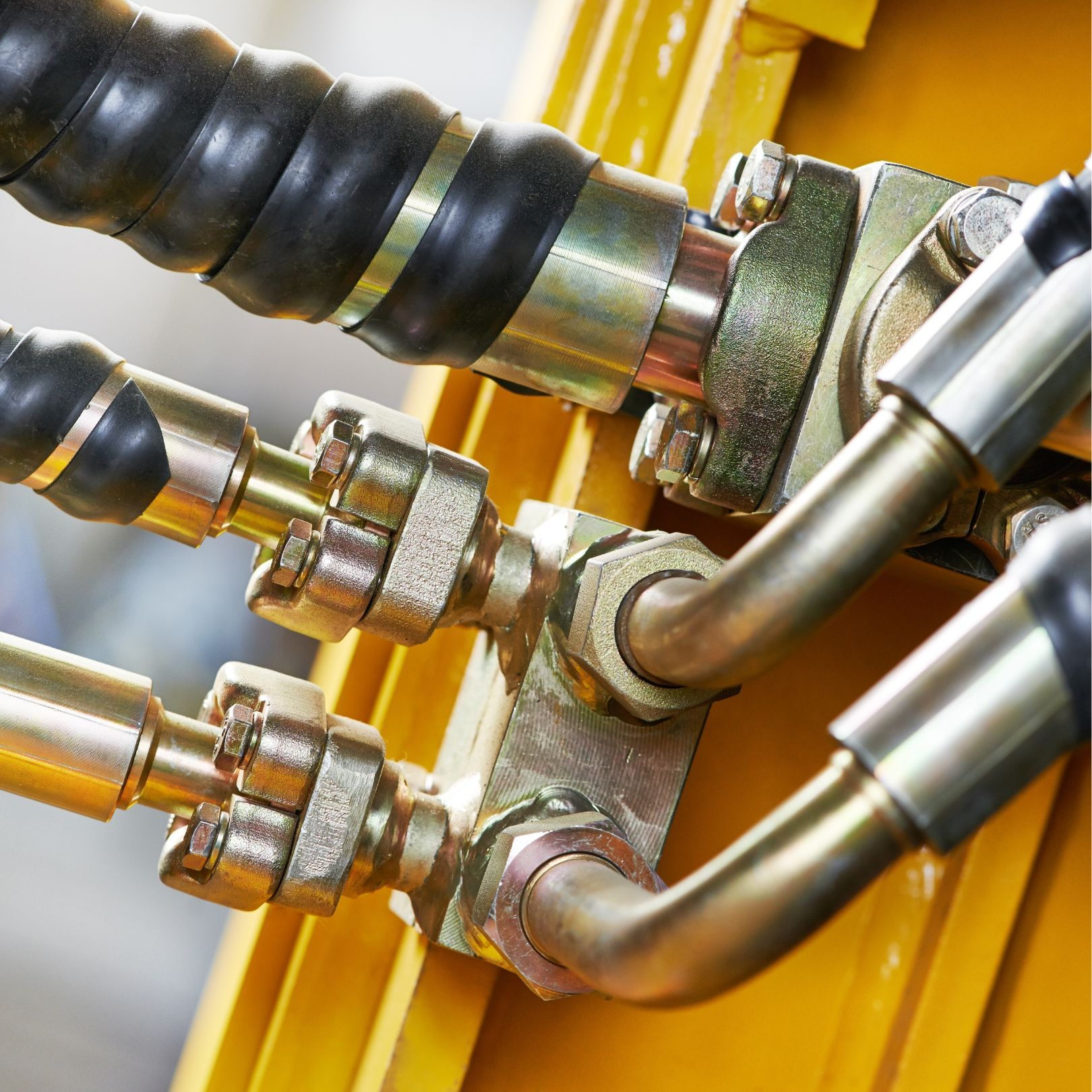 Close-up of metal hydraulic hoses and fittings on a yellow industrial machine