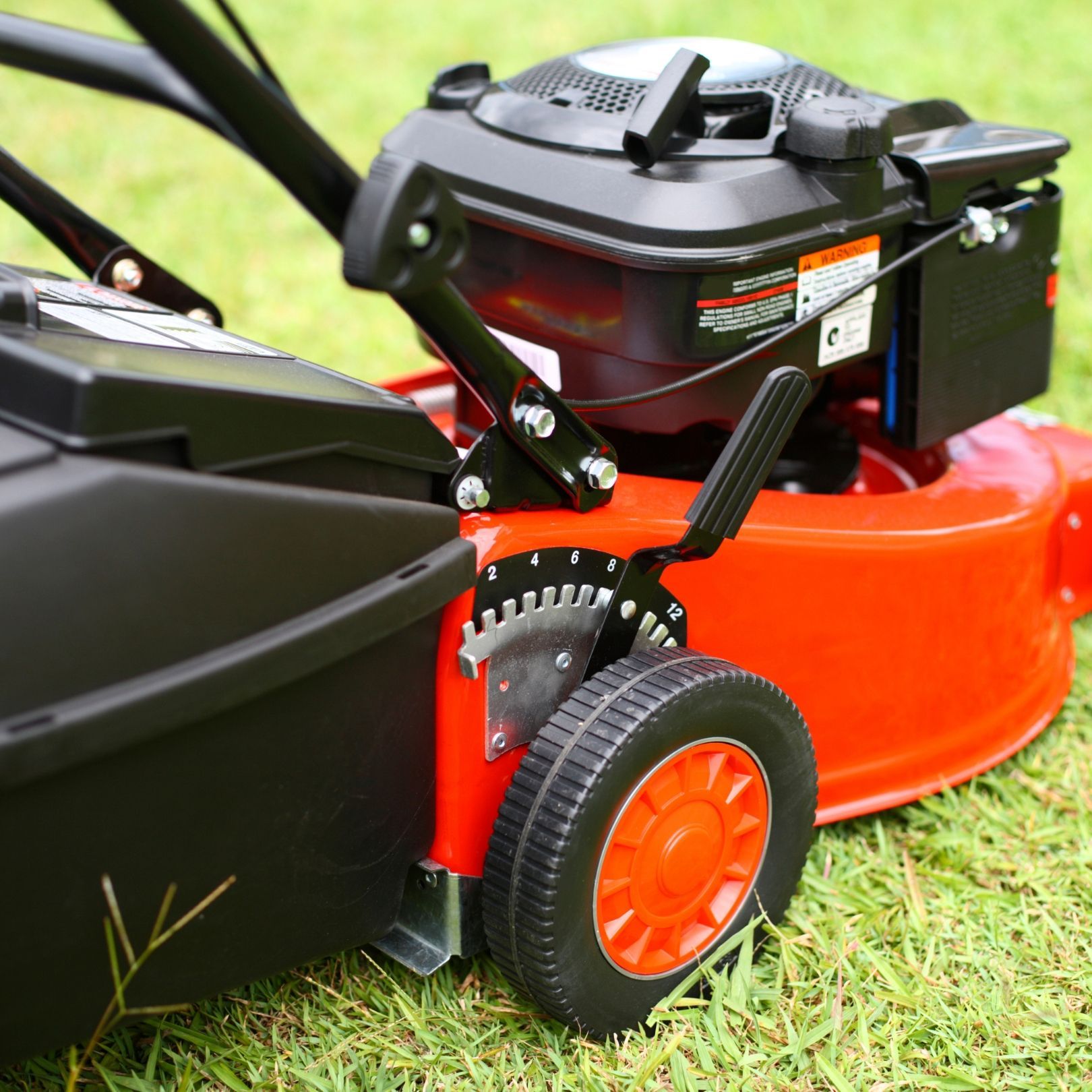 Red lawn mower on grass, showing black engine and orange cutting deck