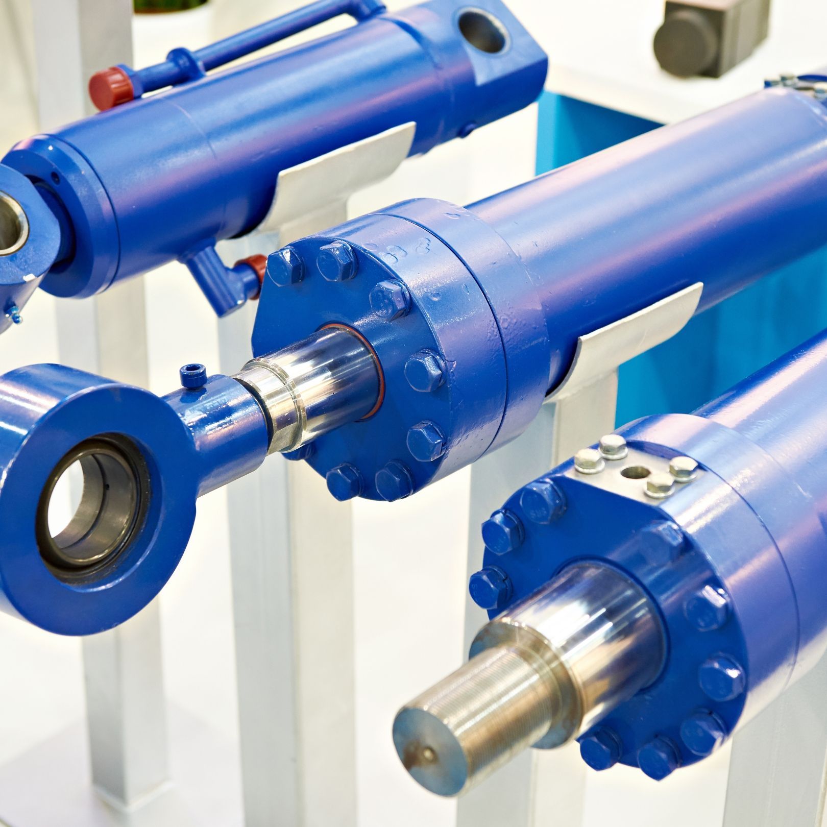 Blue industrial hydraulic cylinders with metal shafts on a white display stand