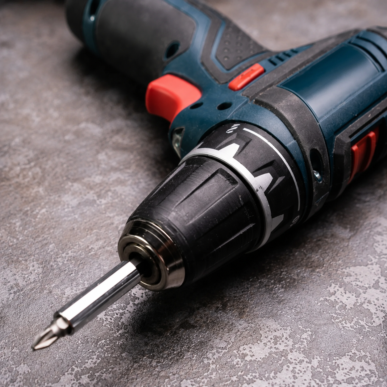 Close-up of a cordless drill with a screwdriver bit on a gray surface