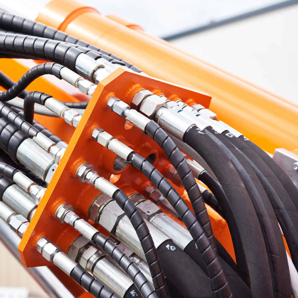 Orange hydraulic hose assembly with black cables and silver fittings in a machine setup