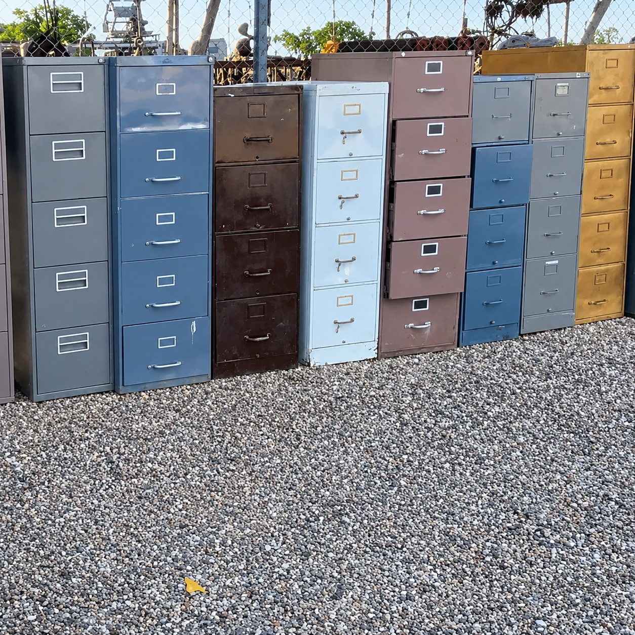 Rows of colorful metal filing cabinets standing outdoors on gravel.