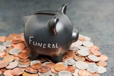 Una alcancía con la palabra funeral escrita en ella está colocada encima de una pila de monedas.