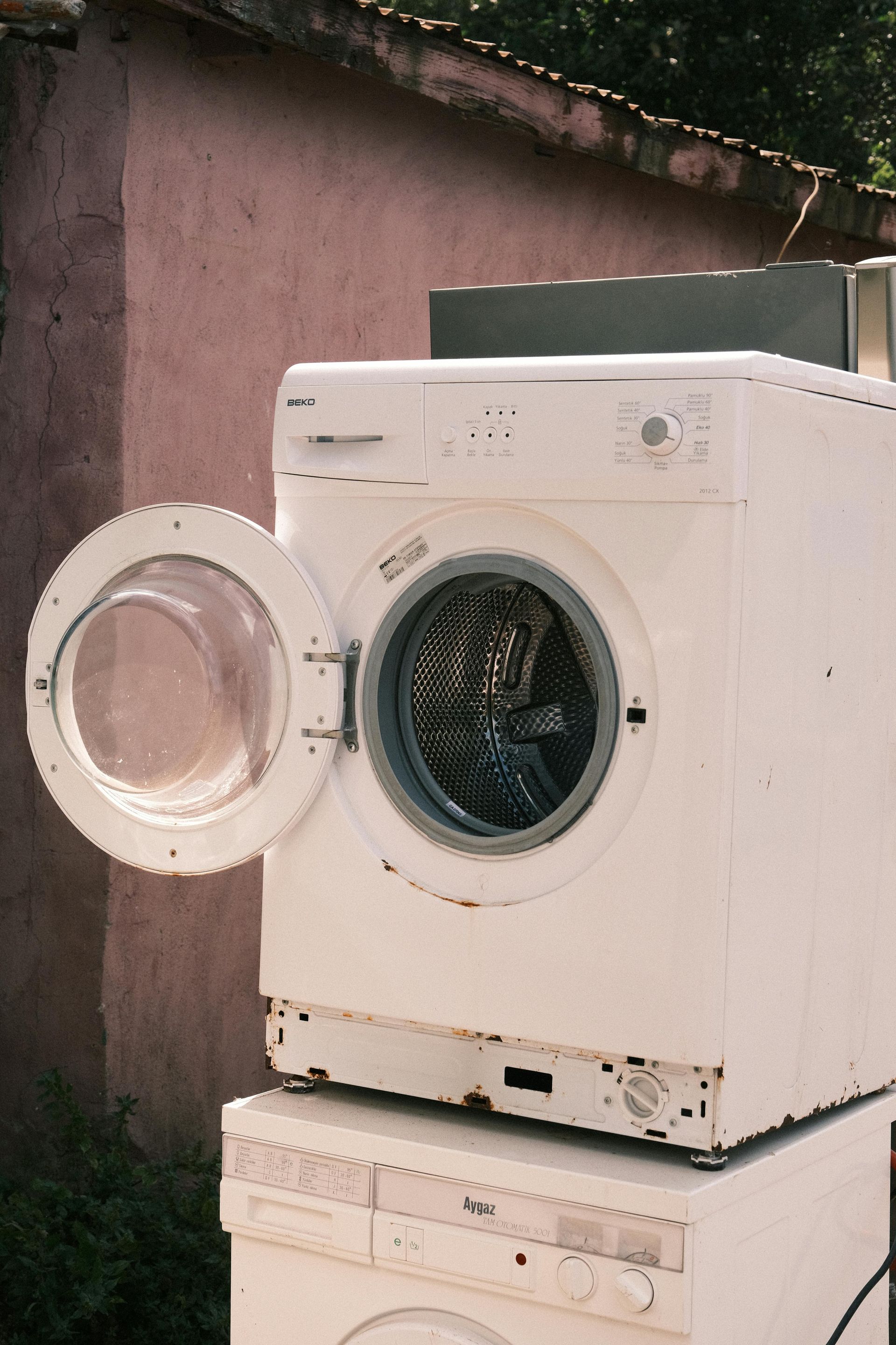 Open front-load washing machine with its door open outdoors against a wall