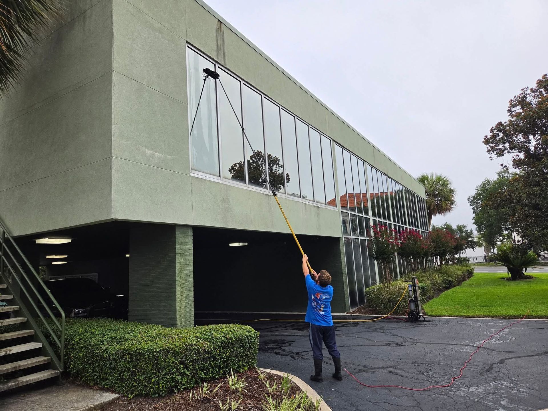 Worker using a long pole to clean second-story windows on a building exterior