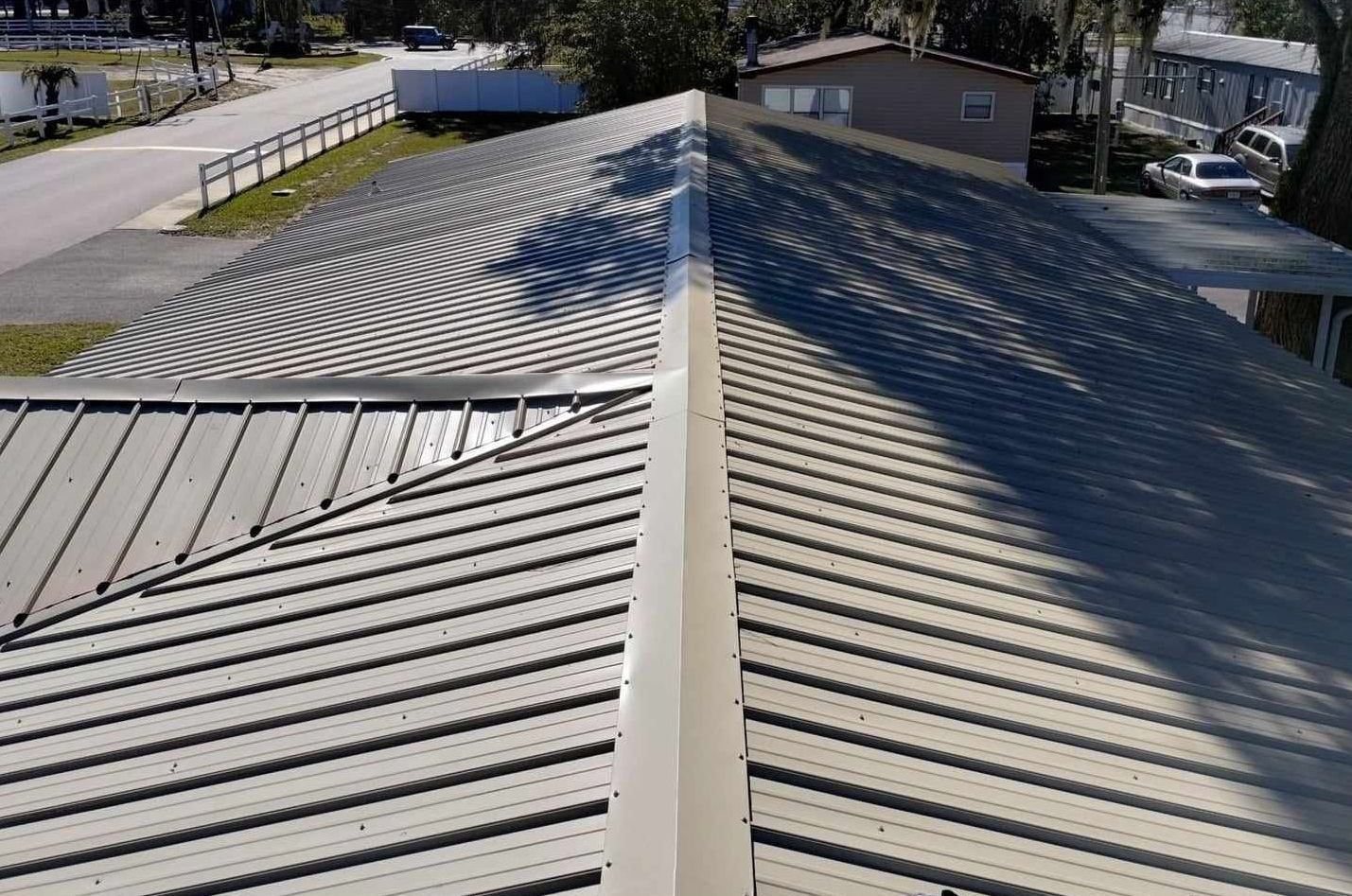 Metal roof with a central ridge, viewed from above, casting strong diagonal shadows in sunlight