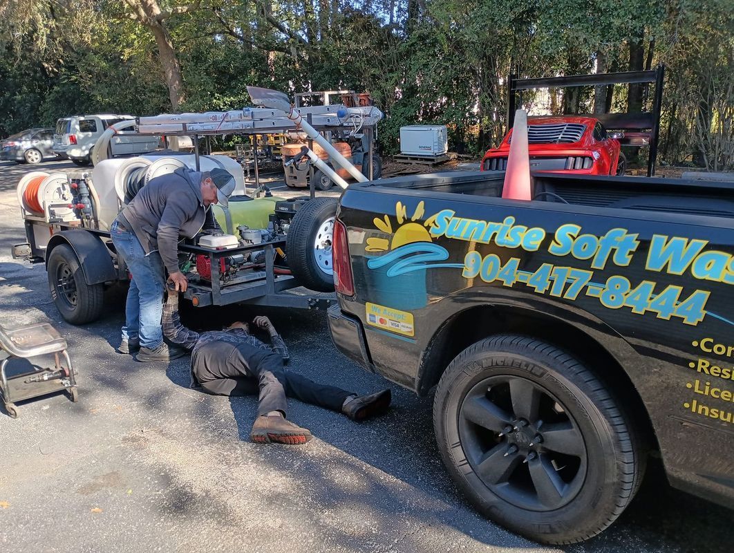 Worker repairs a lawn mower beside a black utility truck with blue and yellow company lettering outdoors