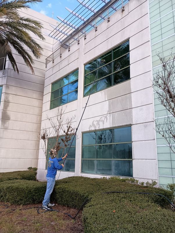 Person in blue stands by shrubs outside a white office building with large windows.