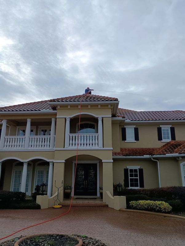 Large cream-colored two-story house with red-tiled roof and white balconies under a cloudy sky