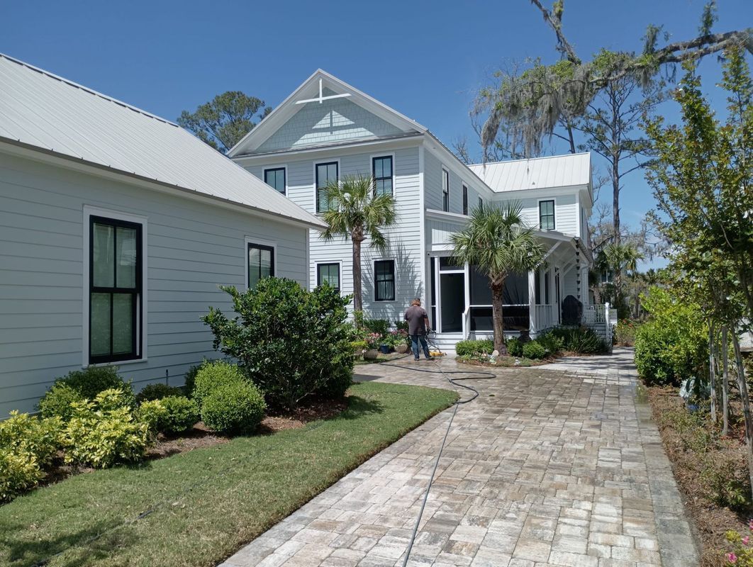 White house with a stone walkway, manicured shrubs, and blue sky in a sunny garden.