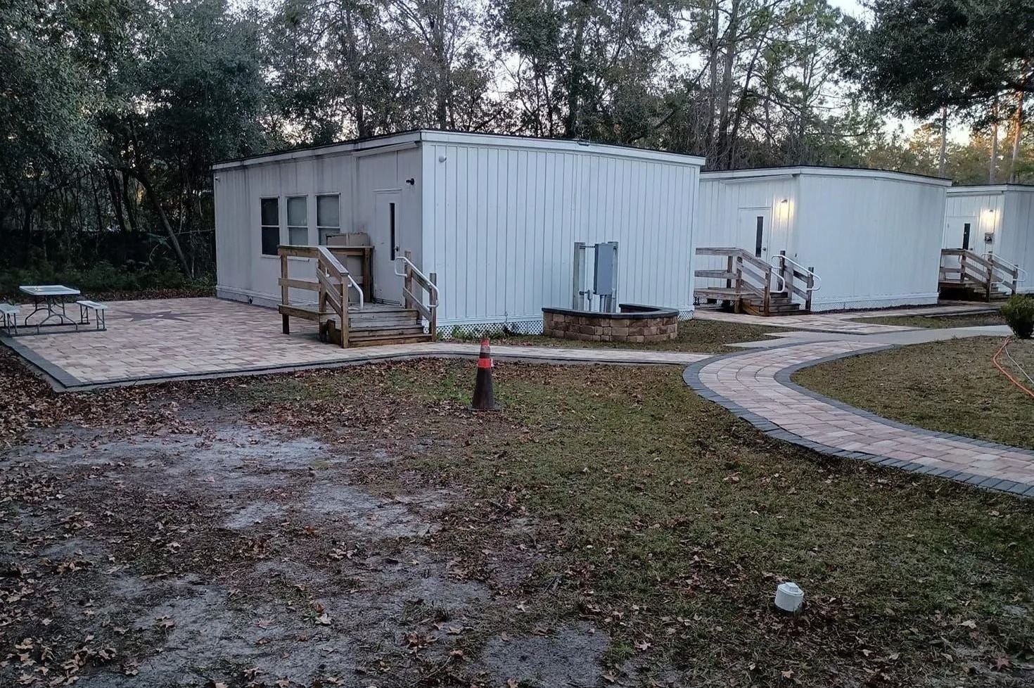 White portable building with stairs and curved gravel path in a wooded outdoor area.