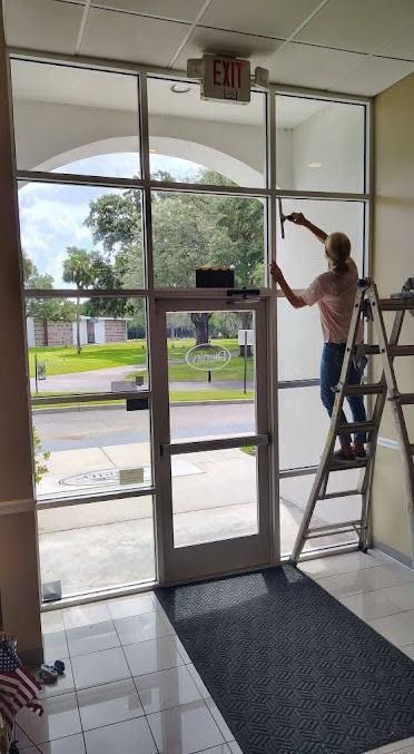 Person on a step ladder painting the upper window frame inside a building entrance.