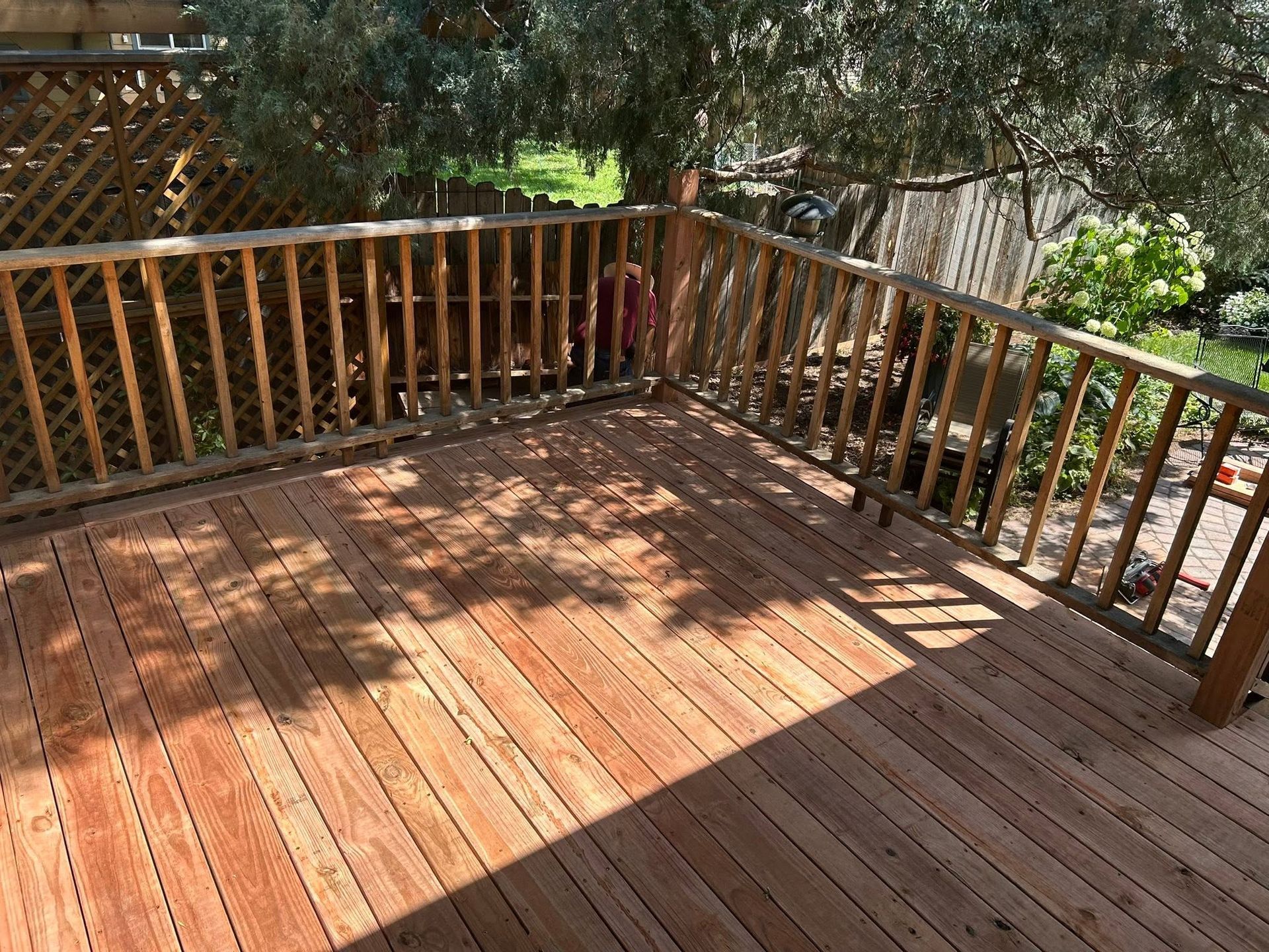 Wooden backyard deck with railings and dappled sunlight from nearby trees