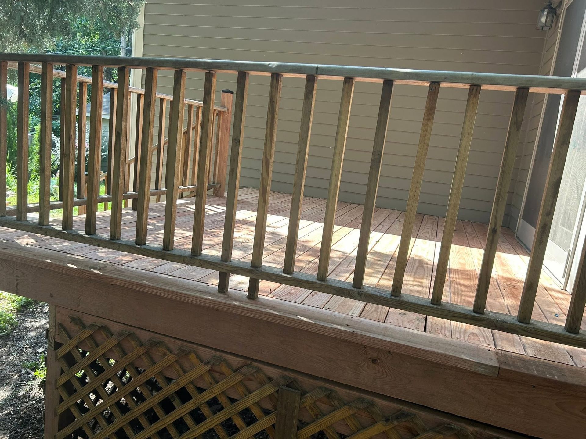 Wooden deck railing with vertical balusters above a lattice-skirted porch in daylight