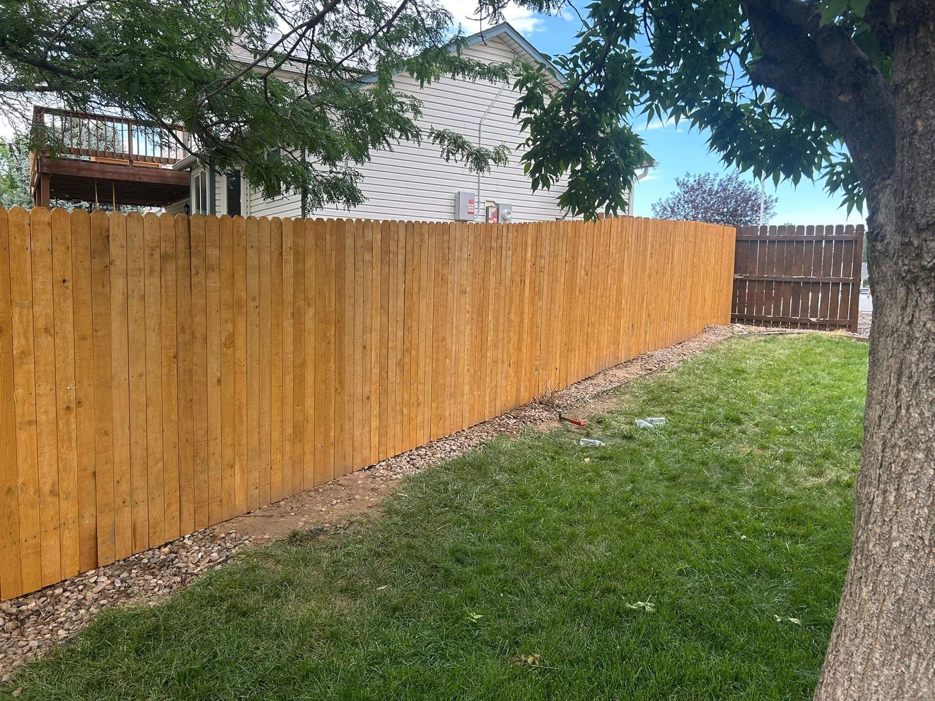 Wooden fence along a grassy sloped yard with trees and a house in the background