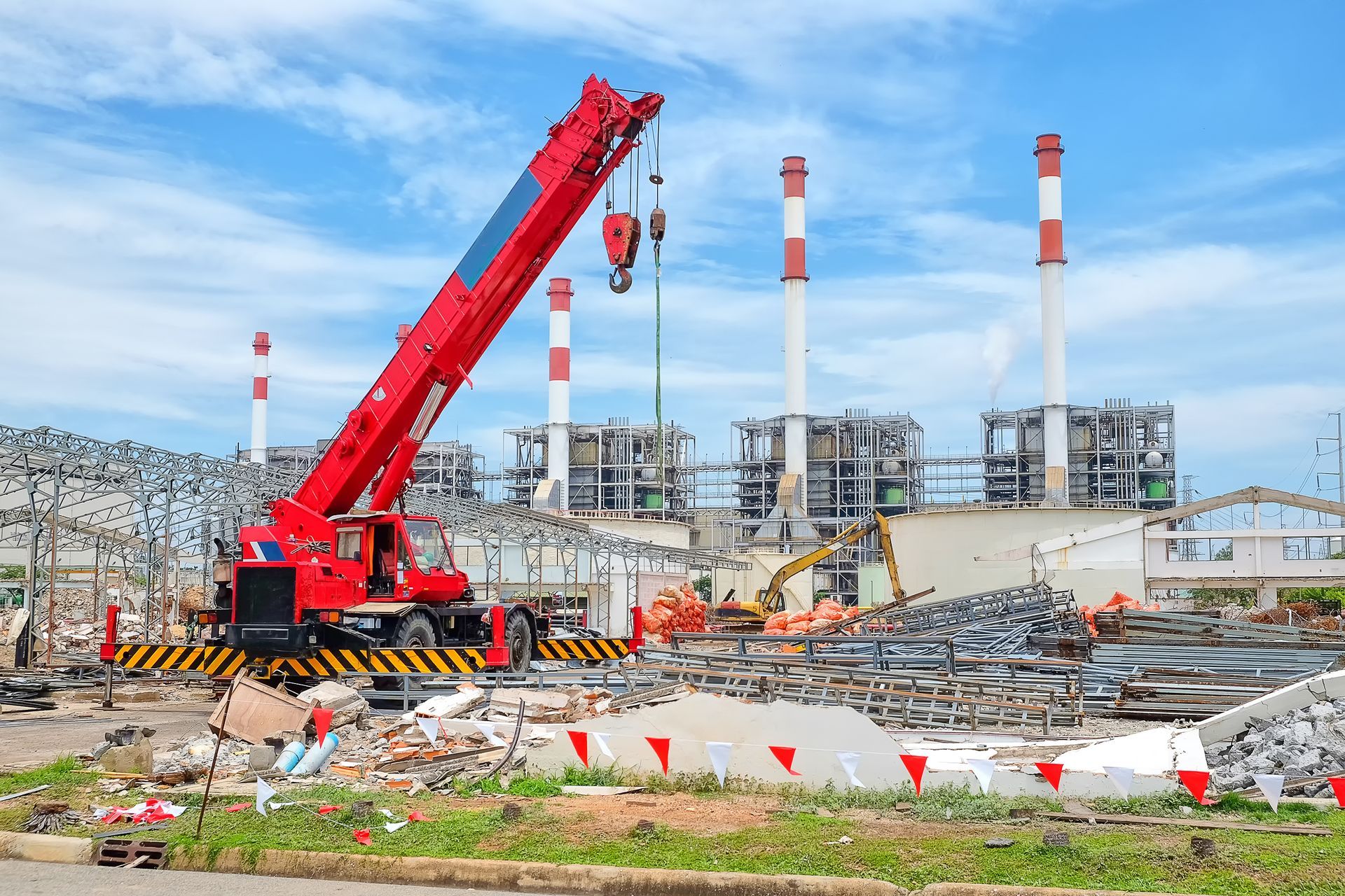 Red crane at a construction site with steel framework and smokestacks in the background