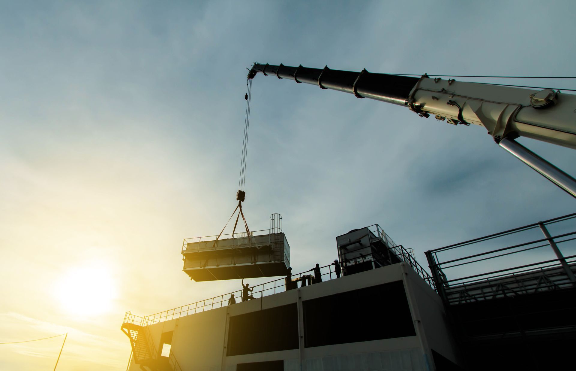 Crane lifting a suspended cargo container above a ship at sunset