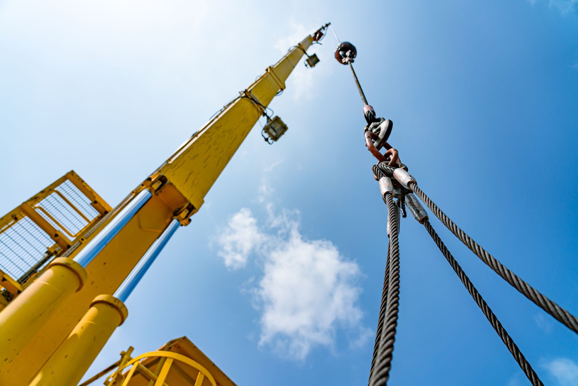 Yellow crane hoisting heavy cables against a blue sky with clouds