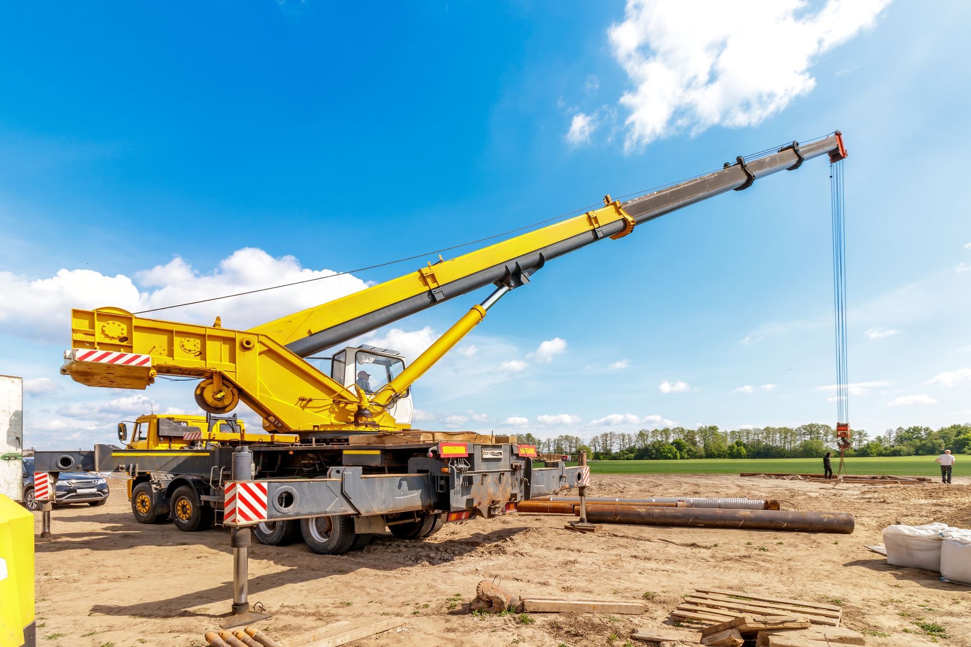 Yellow mobile crane lifting a long beam at a construction site under a blue sky