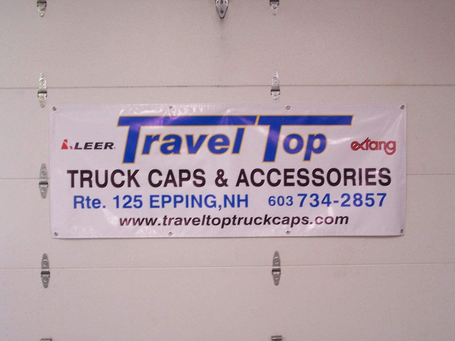 A sign for travel top truck caps and accessories hangs on a garage door