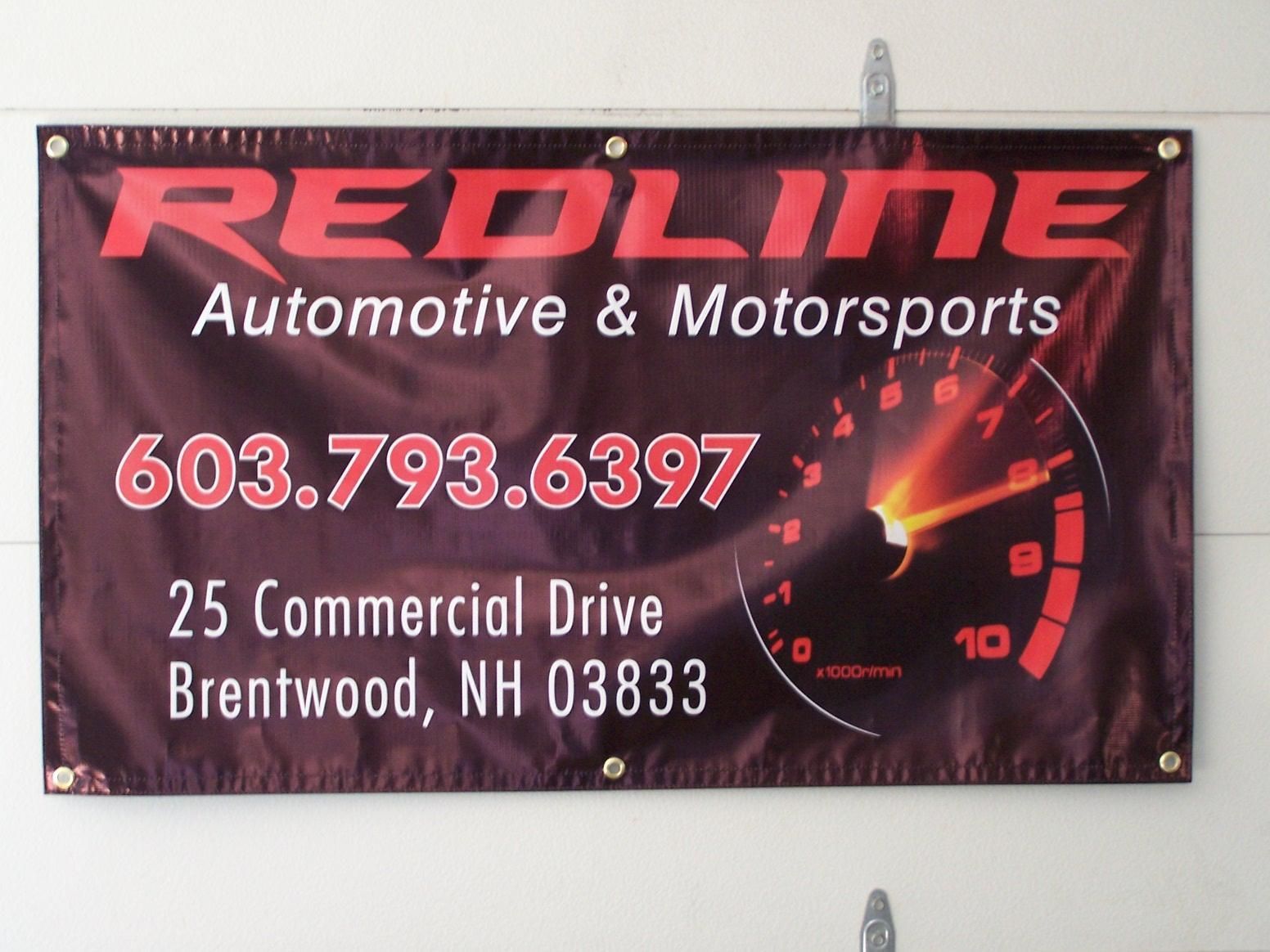A sign for redline automotive and motorsports hangs on a wall